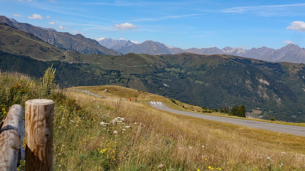 Paved runway leading to the valley below, surrounded by green hills and a blue sky.