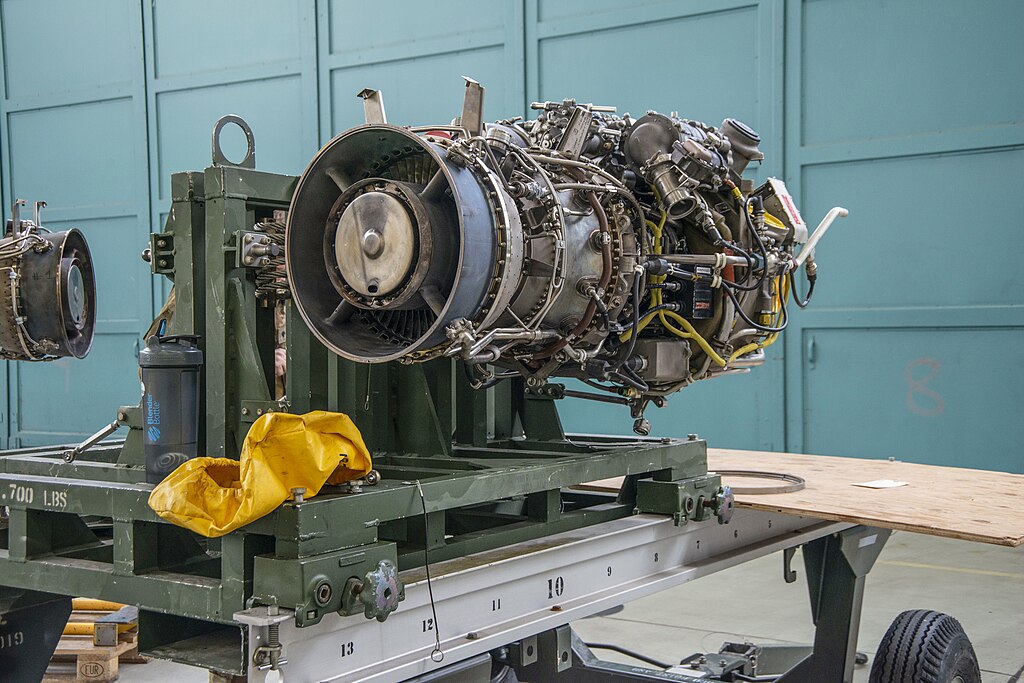 A close-up of a large jet engine mounted on a green metal stand in a workshop, 