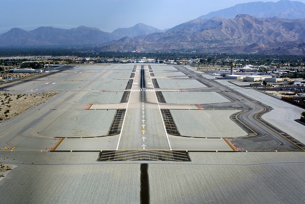 An aerial view of a plam springs airport.straight and paved with a white line down the center and white arrows pointing forward.